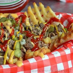 a basket filled with cheesy fries covered in cheese and sauce on top of a checkered table cloth