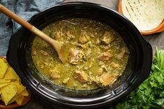 a black crock pot filled with soup next to sliced bread and parsley on the table