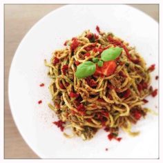 pasta with sun dried tomato pesto on a white plate topped with fresh basil leaves