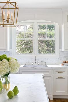 a kitchen with white cabinets and marble counter tops, an island in front of the window