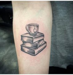 a stack of books with a cup on top of them tattooing someone's arm