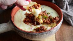 a person dipping some kind of food into a bowl on top of a wooden table