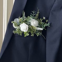 a man wearing a suit with white flowers and greenery on it's lapel