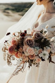 a woman in a wedding dress holding a bridal bouquet on the beach at sunset