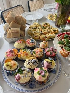 there are many cupcakes on the table with flowers in vases and plates