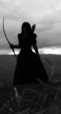 a woman in a long dress is holding a bow and looking at the sky with an arrow