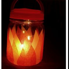 a lit candle in a glass jar on a dark surface with the lid open and lights shining brightly