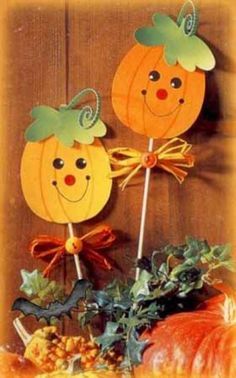 two paper pumpkins with faces on them sitting in front of a wooden wall and some leaves