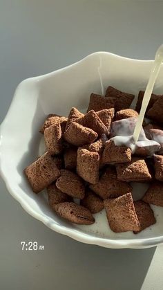 a white bowl filled with brown crumbs and milk being poured on top of them