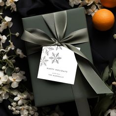 a present wrapped in green paper with a bow on top of it next to oranges and flowers