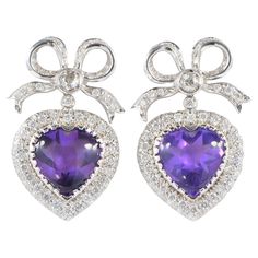 This fine pair of Diamond & Amethyst earrings are 1960 ca. Individually hand fabricated as unique of solid 18 KT white gold Inspired by the Victorian sweet heart jewellery gorgeously modelled with a top bow and a sweet heart swinging down They give a big impact when worn for the beauty of design, workmanship and gemstone glow Hearts centre are two superb rich Purple natural Amethysts of 20.00 CT for both – complemented by 2.70 Ct of round cut Diamonds varying in size to fit the design Diamonds rated between G VVS/ SI – Supreme white and richly sparkly Earrings measure 33 mm. x 20 mm. They are made for pierced ears Excellent condition They are truly WOW! Gold weight is 15.4 grams Metal: 18 Kt white gold Hallmarks: assay Gems: 2 heart cut natural Amethyst totalling approx 20.00 Ct (12.7 mm. Sparkly Earrings, Bow Earrings, European Cut Diamonds, Amethyst Earrings, Vintage Diamond, High Jewelry, Heart Jewelry, Round Cut Diamond, Brilliant Cut Diamond