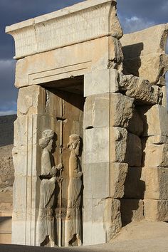 two statues are standing in front of a stone structure with an open door that leads to another one