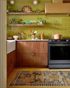 a kitchen with green tiled walls and wooden cabinetry, an oven and rug on the floor