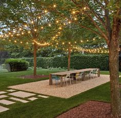 an outdoor dining area is lit up with string lights and trees in the back yard