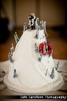 a wedding cake is decorated with white frosting and snow - covered trees, as well as a bride and groom on top