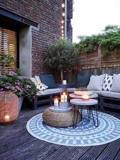 an outdoor living area with couches, tables and candles on the ground in front of a brick wall