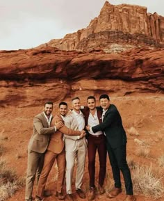 four men posing for a photo in front of a rock formation, with one holding his arm around the other's neck