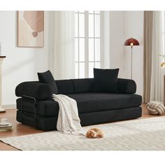 a black couch sitting on top of a wooden floor next to a rug and window