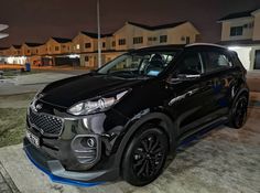 a black car is parked in front of some houses at night with its lights on