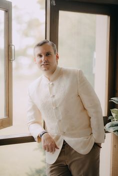 a man standing in front of a window wearing a white jacket and khaki pants