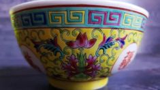 a yellow and red bowl sitting on top of a table next to a purple wall