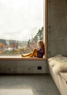 a woman sitting on a window sill looking out at the trees outside her bedroom