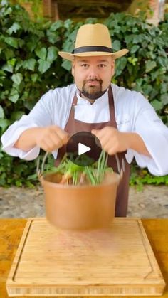 a man wearing an apron and hat is holding a pot with plants in it on a table