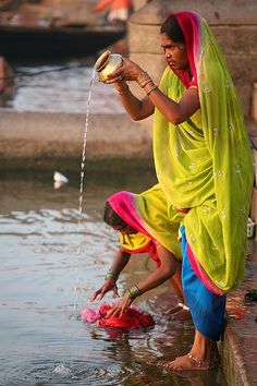 two women in sari washing their hands and feet at the edge of a body of water