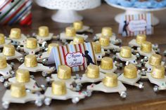 a table topped with lots of gold and white hats on top of small plates filled with candy