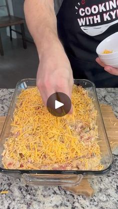 a person adding cheese to a casserole in a glass dish on top of a counter