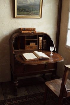 an old desk with books and a wine glass on it in front of a painting