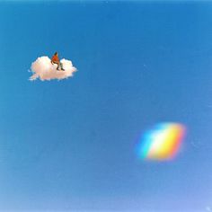 a bird sitting on top of a cloud with a rainbow in the sky behind it