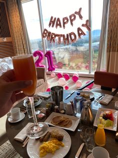 a table with food and drinks on it in front of a large window that says happy birthday