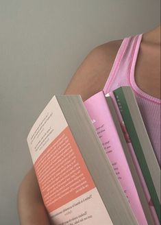 a woman is holding two books in her hands and looking at the camera while wearing a pink tank top