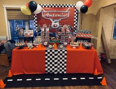 an orange table topped with lots of desserts and balloons in front of a checkerboard backdrop