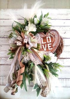 a heart shaped wreath with feathers and flowers on a white wooden background that says love