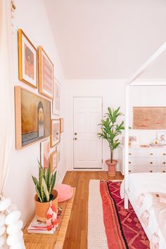 a bed room with a neatly made bed next to a plant and pictures on the wall