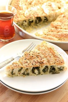 a slice of quiche with spinach and cheese on a plate next to a cup of tea