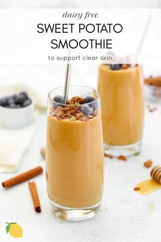 two glasses filled with smoothie on top of a white table next to cinnamon sticks