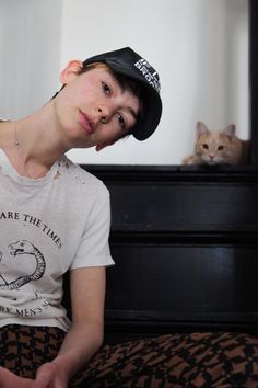 a young man sitting on top of a bed next to a brown and white cat