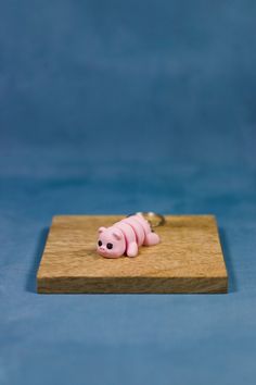 a pink pig keychain sitting on top of a piece of wood with a blue background