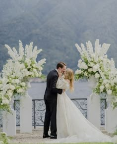 a bride and groom kissing in front of an archway with white flowers on the side