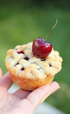 a hand holding a small pie with a cherry on it's top and a bite taken out