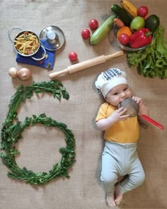 a baby laying on top of a table next to vegetables and other items that include pasta