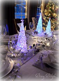 a dining room table set for christmas with blue and white lights on the trees in the background