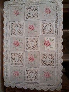 a white crocheted blanket with pink flowers and leaves on the edges, hanging from a wall