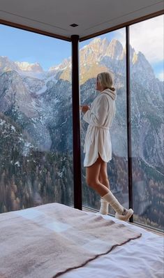 a woman standing on top of a bed in front of a window looking out at mountains