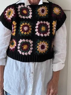 an older woman wearing a black and multicolored crocheted sweater with flowers on it