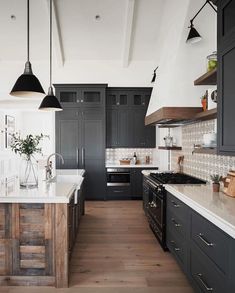 a large kitchen with black cabinets and white counter tops, wooden flooring and hanging lights