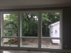 an empty room with three large windows overlooking the yard and trees in the back ground